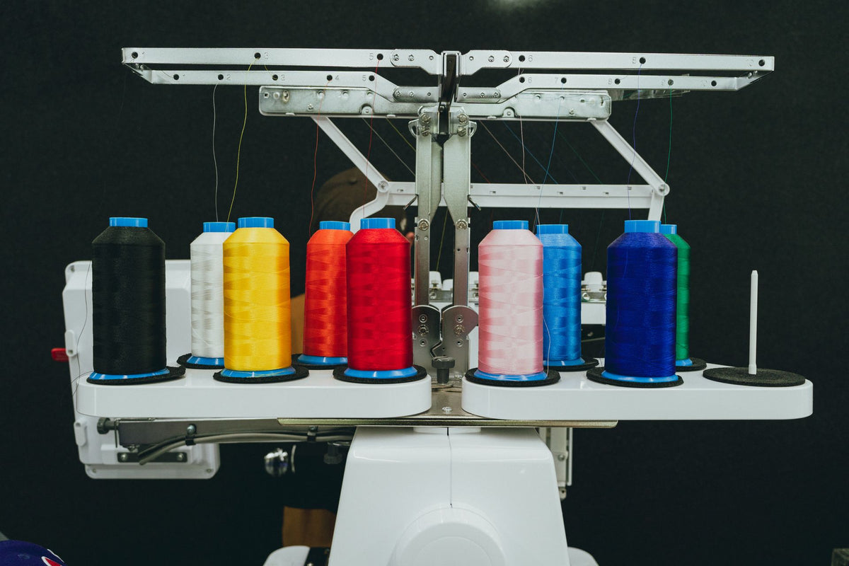 Cônes de fil colorés sur une machine à broder industrielle, la technique comparée au transfert DTF pour un tablier cuisinier personnalisé