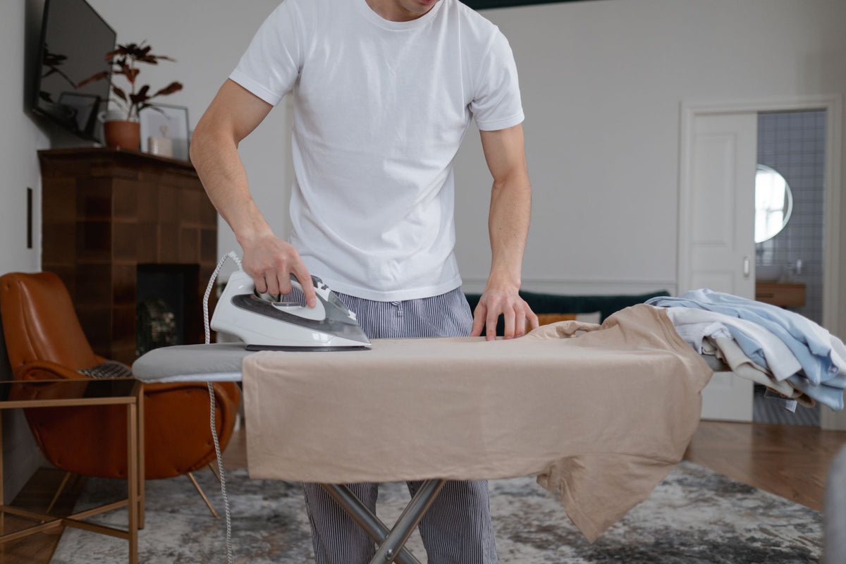 Homme repassant un t-shirt au fer à repasser sur une planche, dans un salon