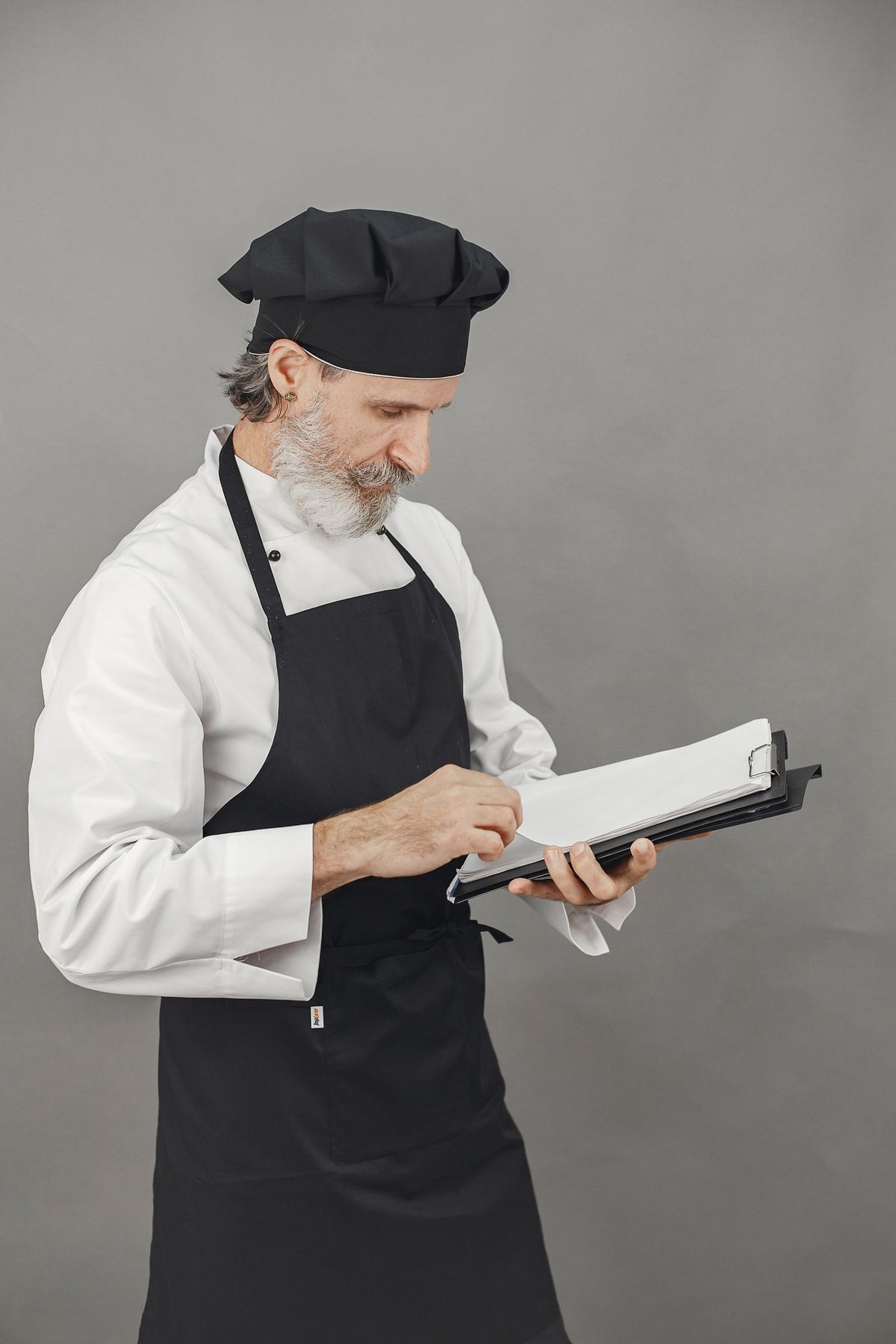 Chef en veste blanche portant un tablier à bavette noir, uniforme de cuisine professionnelle