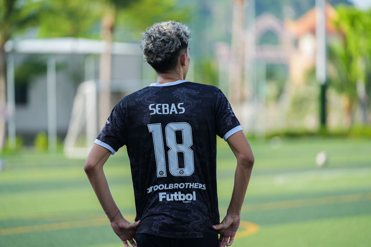 Dos d'un maillot de foot noir floqué du nom SEBAS et du numéro 18, sur un terrain