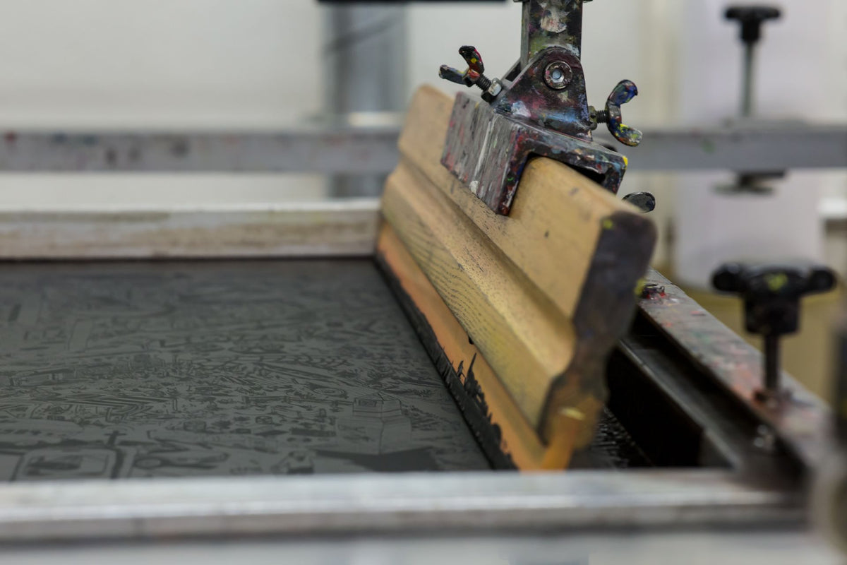 Écran de sérigraphie tendu sur son cadre et raclette en bois, sur une presse d'atelier d'impression textile