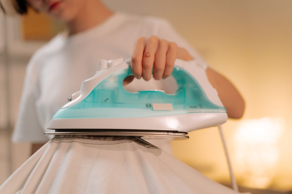 Personne repassant un tissu blanc avec un fer à repasser classique, le geste utilisé pour poser un transfert DTF ou flex à la maison